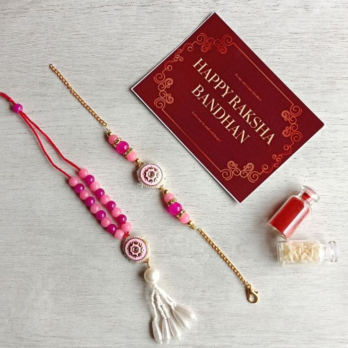 pink pearl meenakari rakhi set for bhaiya bhabhi placed on grey sheet with roli chawal bottle and Rakshabandhan card 