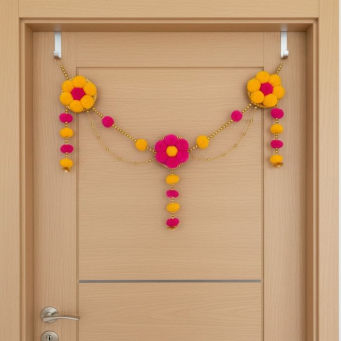 yellow - pink pompom toran hanging on cream colored door