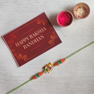 bro-sis cartoon rakhi placed on off-white sheet with roli chawal and Rakshabandhan card 