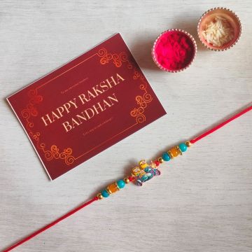 minion rakhi for kids placed on off-white sheet with roli chawal and rakshabandhan card 